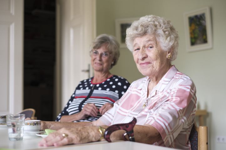 Zwei ältere Damen Rentnerinnen Seniorinnen sitzen an einem gedeckten Kaffeetisch und lächeln in die Kamera