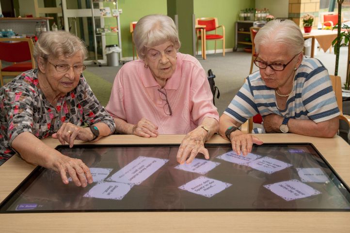 Drei Senioren spielen Karten auf einem großen Bildschirm