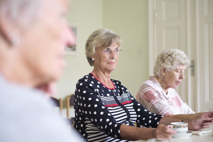 Ältere Frauen sitzen um einen Tisch, unterhalten sich und trinken Kaffee, Seniorinnen