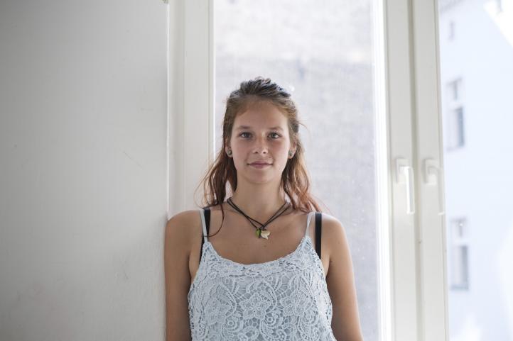 Ein junges Mädchen steht im Treppenhaus mit dem Rücken zum Fenster und lehnt sich am Fenstersims an