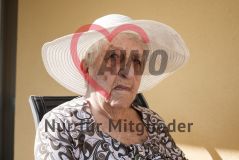 Eine alte Frau Seniorin mit Hut sitzt auf einem Balkon und blickt in die Kamera