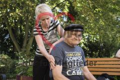 Eine Frau massiert einem alten Mann Senior draußen auf einer Bank